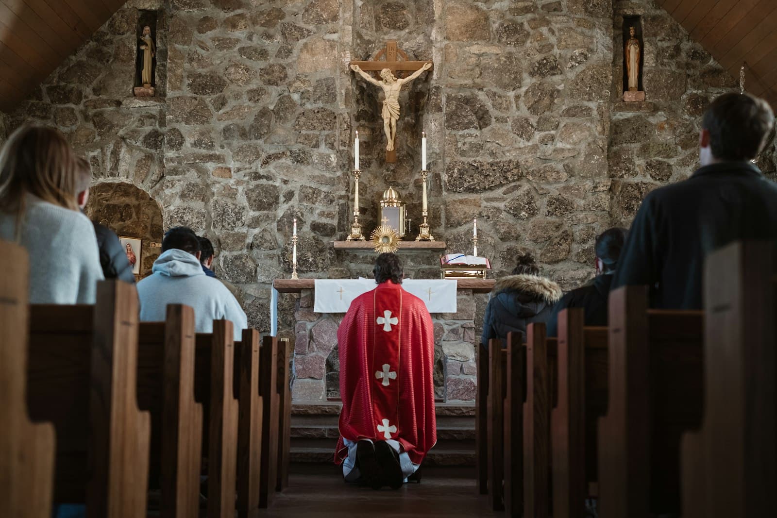 A priest in red vestments kneeling before the altar of a stone chapel during Mass